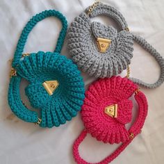 three crocheted purses sitting next to each other on a white sheet with gold hardware