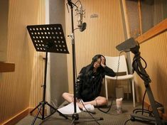 a woman sitting on the floor in front of a microphone and recording equipment with her legs crossed