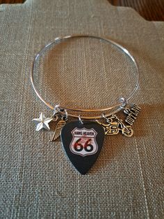 "Fun charms and a Route 66 guitar pick make up this stainless adjustable bangle bracelet. The bangle expands to slide over the hand but fits a 7\" wrist best" Adjustable Silver Jewelry For Concert, Adjustable Silver Jewelry For Concerts, Guitar Pick Bracelet, Adjustable Metal Music-themed Jewelry, Adjustable Silver Bracelets For Concerts, Adjustable Music-themed Jewelry For Concerts, Adjustable Bracelet Jewelry For Concerts, Adjustable Nickel-free Stainless Steel Bangle, Adjustable Stainless Steel Nickel-free Bangle