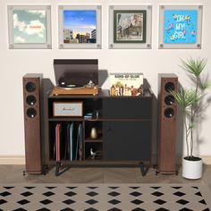 a computer desk with speakers and pictures on the wall in an empty room next to a potted plant