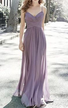 a woman in a long purple dress standing on the street with her hands behind her back