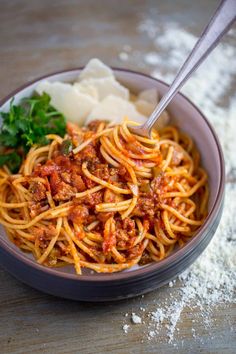 a bowl filled with spaghetti and sauce on top of a wooden table next to mashed potatoes