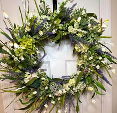 a wreath with flowers and greenery hanging on the front door to welcome people into the house