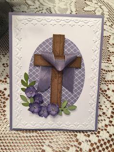 a card with a cross and purple flowers on the front, sitting on a table