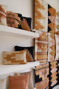 several decorative pillows are on shelves in a room that is white and has many different colors