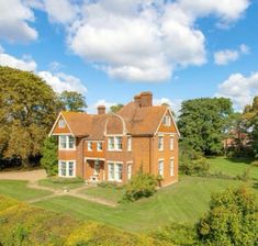 an aerial view of a large red brick house in the middle of a lush green field