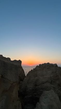 the sun is setting over the ocean and rocks