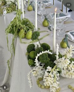 the table is set with green and white flowers, pears, greens and candles