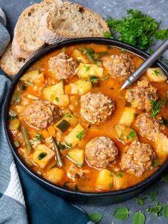 a bowl of meatball soup with bread and parsley on the side, ready to be eaten