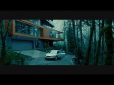 a white car parked in front of a house surrounded by trees and bushes on a rainy day