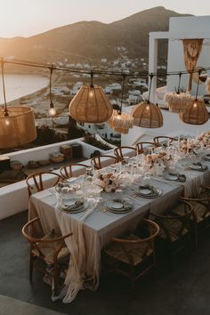 an outdoor dining table set up with plates and silverware on it, overlooking the ocean