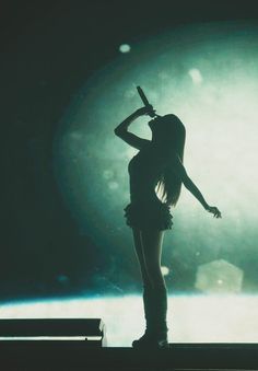 a woman standing in front of a stage holding a microphone up to her head with both hands