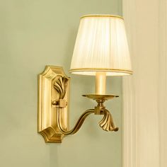 a gold wall light with a white shade on it's side and a green wall in the background