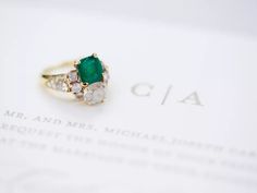 an emerald and diamond ring sitting on top of a piece of paper with the word cia written below it