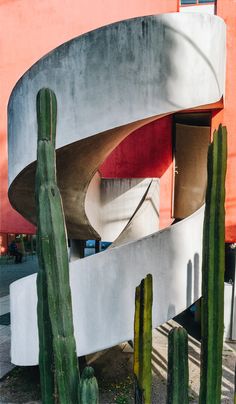 an unusual building with cactus in front of it and a red wall behind the building