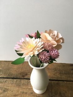 a white vase filled with flowers on top of a wooden table