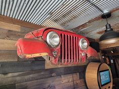 an old red jeep hanging from the ceiling in a garage with wood planks and metal roofing