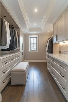 a large walk - in closet with white cabinets, drawers and an ottoman on the floor