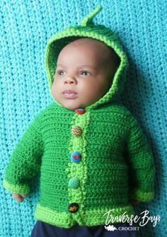 a baby is wearing a green crocheted jacket and pants with buttons on the hood