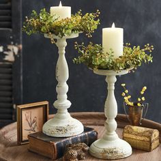 two white candles sitting on top of a table next to an old book and some flowers