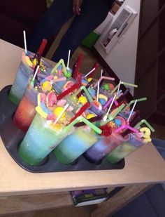 there are many different colored drinks in the cups with straws and candy on them