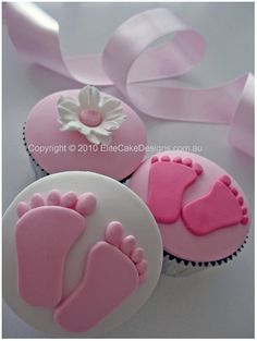 three cupcakes decorated with pink icing and baby feet on top of each one