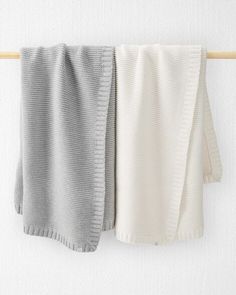 two knitted blankets hanging on a clothes line, one white and the other grey