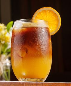 an orange slice sits on top of a drink in a glass next to some flowers