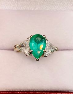 an emerald and diamond three stone ring in a velvet box with red velvet lining around it