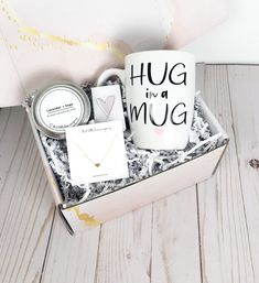 a gift box containing a mug and some other items on a white wooden table with a pink painted background