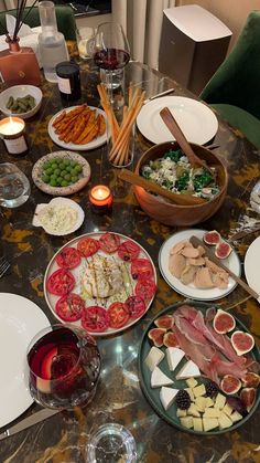 a table filled with plates and bowls of food next to wine glasses, candles and utensils