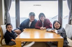 three adults and two children sitting at a wooden table in front of a large window