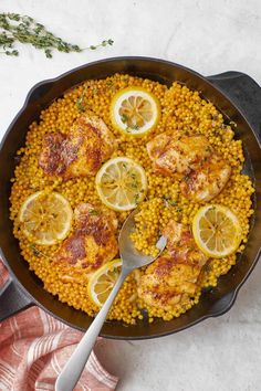 a skillet filled with chicken, corn and lemons on top of a table