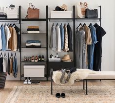 an organized closet with clothes, shoes and handbags hanging on the wall next to a bench