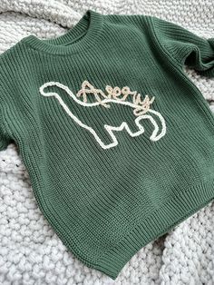 a green sweater with the word happy on it is laying on a white knitted blanket