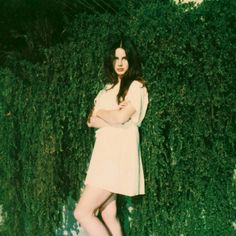 a woman standing in front of a green wall with her arms crossed and legs crossed