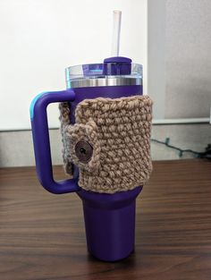 a purple coffee cup with a crocheted handle and lid on a wooden table