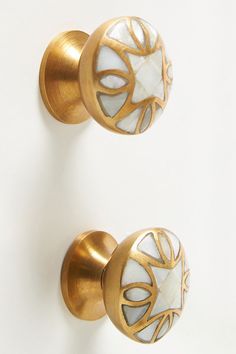 two white and gold door knobs with designs on them, against a white background