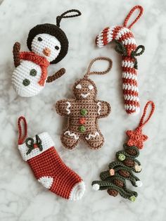 crocheted christmas ornaments are arranged on a marble countertop, including one snowman and two gingerbreads