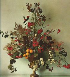 a vase filled with flowers and fruit on top of a wooden table next to a wall