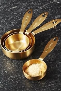 four gold measuring cups and spoons with personalized names on the handles, sitting on a granite countertop