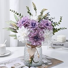 a vase filled with purple and white flowers sitting on top of a table next to books