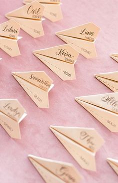 a pink table topped with lots of gold paper airplane shaped place cards on top of each other