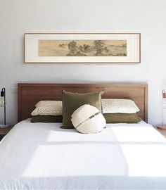 a bed with white sheets and pillows in a bedroom next to a painting on the wall