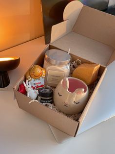 an open box on a table with candles and other items in it next to a lamp