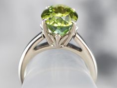 This classically designed green tourmaline solitaire ring is timeless and goes with everything! This simple and elegant ring features a polished white gold mounting. The green tourmaline is a rich lime green, beautifully protected in the simple four-prong setting.Metal: 14K White GoldGem: Green Tourmaline 5.38 CaratsGem Measurements: 12.8 x 9.4 mm, OvalRing Size: 6.50Marks: “SGI 14K” Stamped on the inside band Classic Peridot Jewelry With Brilliant Cut, Elegant Tourmaline Solitaire Ring, Classic Green Tourmaline Jewelry, Classic Green Jewelry With Tension Setting, Classic Solitaire Peridot Ring, Classic Tourmaline Ring With Prong Setting, Modern Green Rings With Prong Setting, Classic Peridot Rings With Prong Setting, Formal Green Ring With Tension Setting