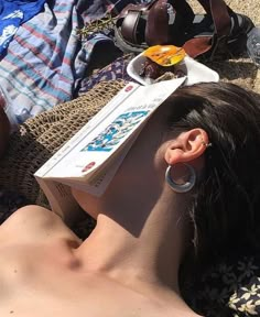 a woman laying on top of a beach next to an open book and earring