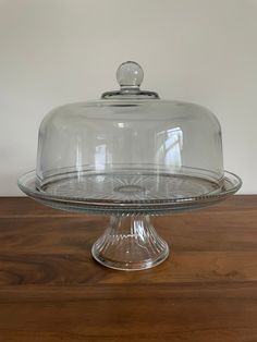 a glass cake plate with a domed cover on it's top, sitting on a wooden table