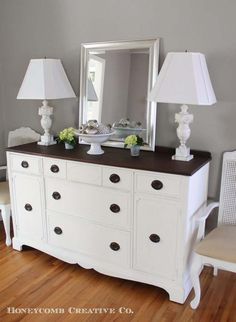 a white dresser sitting on top of a hard wood floor next to a lamp and mirror