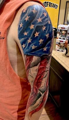 a man with an american flag tattoo on his arm and shoulder is standing in front of a counter